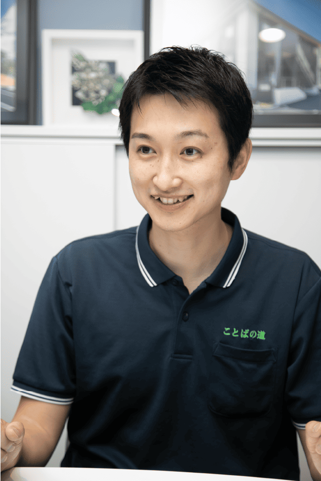 ことばの道スタッフ・総括責任者・安居和輝 黒髪で単発の清潔感のある男性言語聴覚士が白い背景を前ににこやかに話している