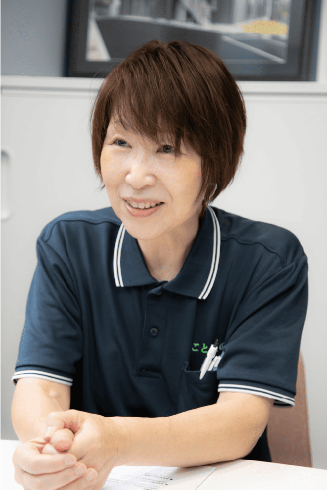 ことばの道スタッフ・代表理事・安居道子 ショートカットの清潔感のある優しげな女性が白い背景を前に話している