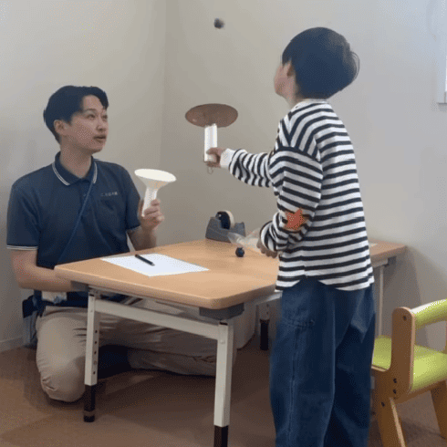 児童発達支援「表現・感性を育む」言語聴覚士と子どもが作成した工作でボール飛ばしで遊んでいる