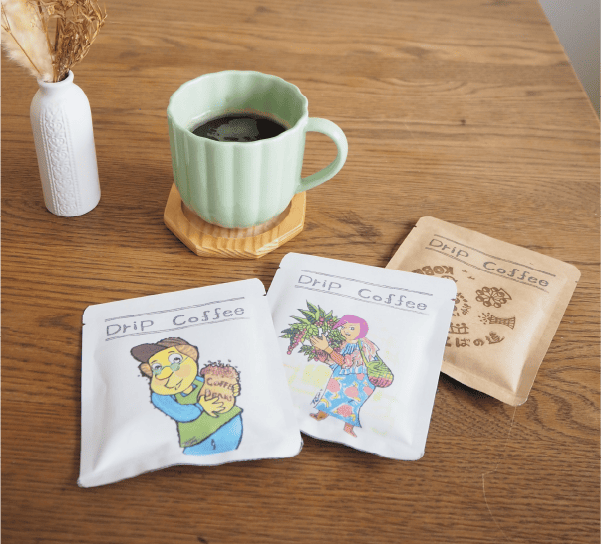 神戸市須磨区焙煎コーヒーの就労支援 大好評のオリジナルイラスト入りパッケージのラインナップとコーヒーがテーブルに並んでいる